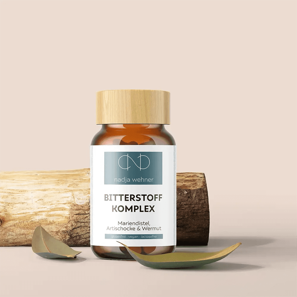 Eine „Bitterstoff Komplex“-Flasche von Nadja Wehnert mit Holzverschluss wird elegant auf einem neutralen Hintergrund mit Blättern präsentiert. Diese Mischung enthält Mariendistel-Essenz, um ihre natürlichen Eigenschaften zu verstärken. Marke: Rosen Apotheke Manufaktur.